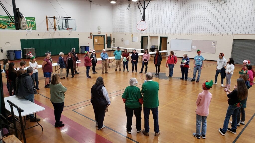 People in holiday themed clothes and hats standing in a circle in a gymnasium. 