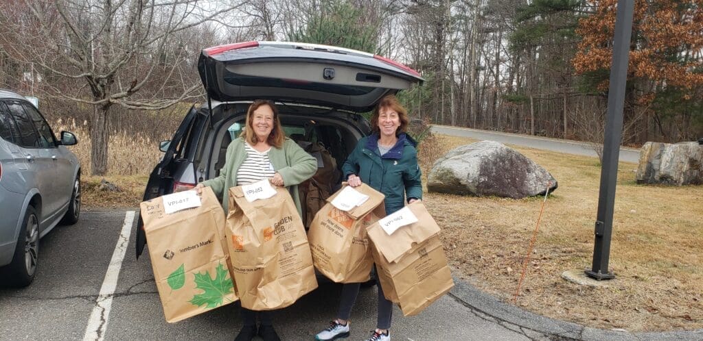 Two smiling women unloading bags of presents from their car. 