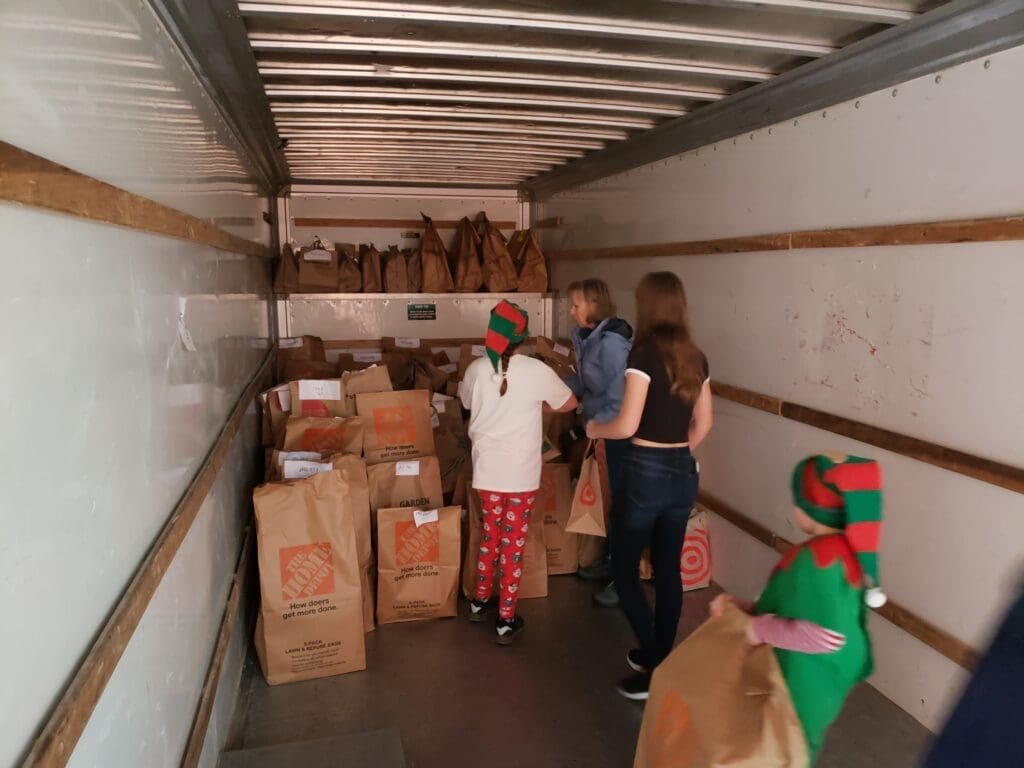 Two children in elf costumes helping adults load the inside of a large truck